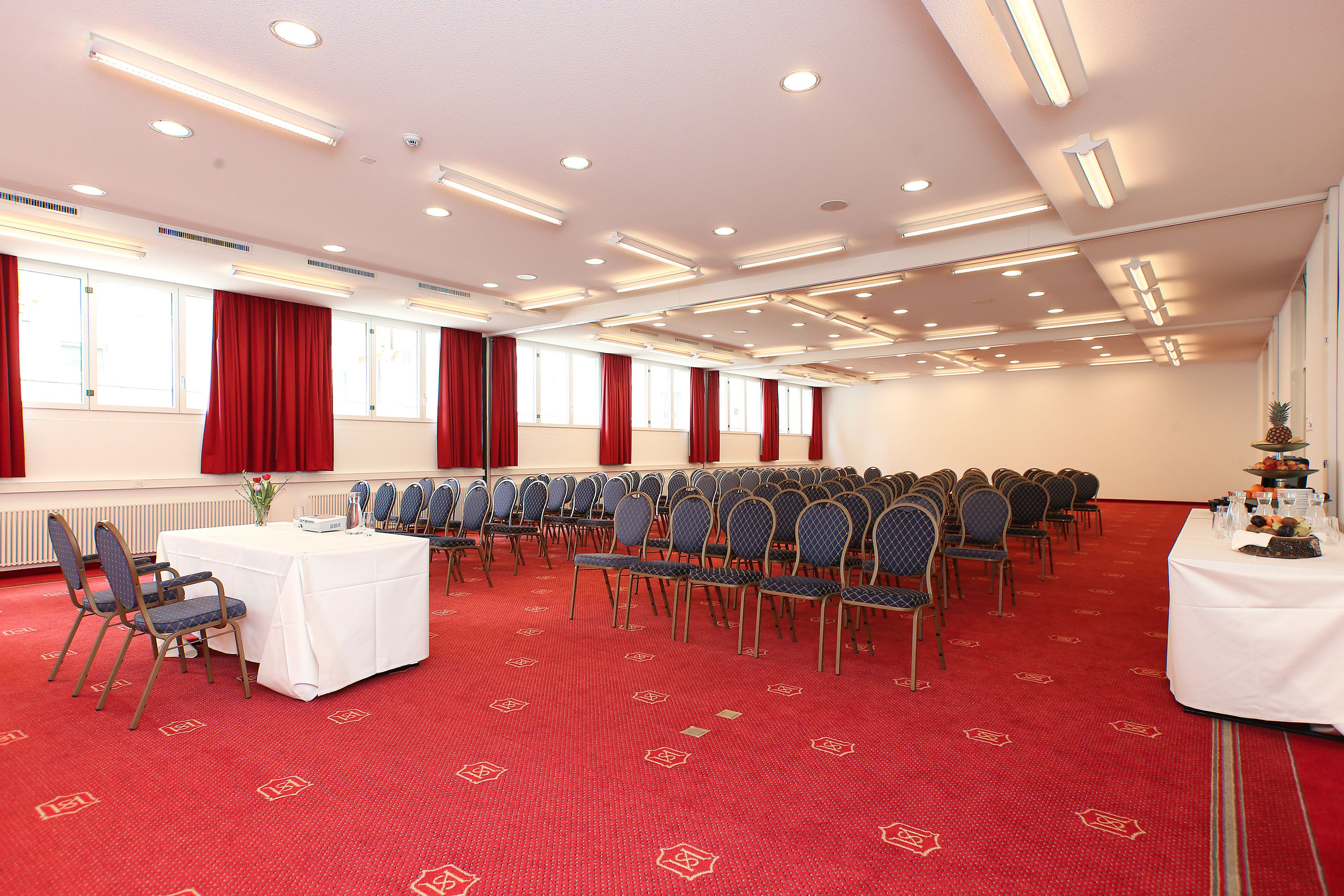 A conference room with rows of chairs, a white table, and red curtains.