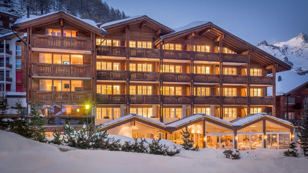 A multi-story wooden lodge with balconies and large windows, surrounded by snow. - Hotel Schweizerhof Gourmet & Spa (Saas-Fee)
