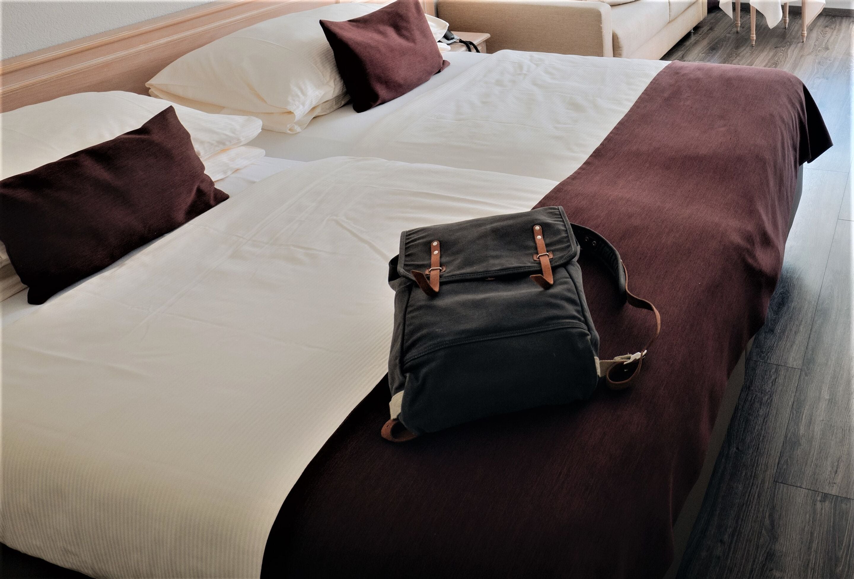 Un lit bien fait, recouvert d’une couverture marron foncé, avec un sac noir posé dessus.
