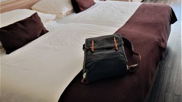 Un lit bien fait, recouvert d’une couverture marron foncé, avec un sac noir posé dessus.