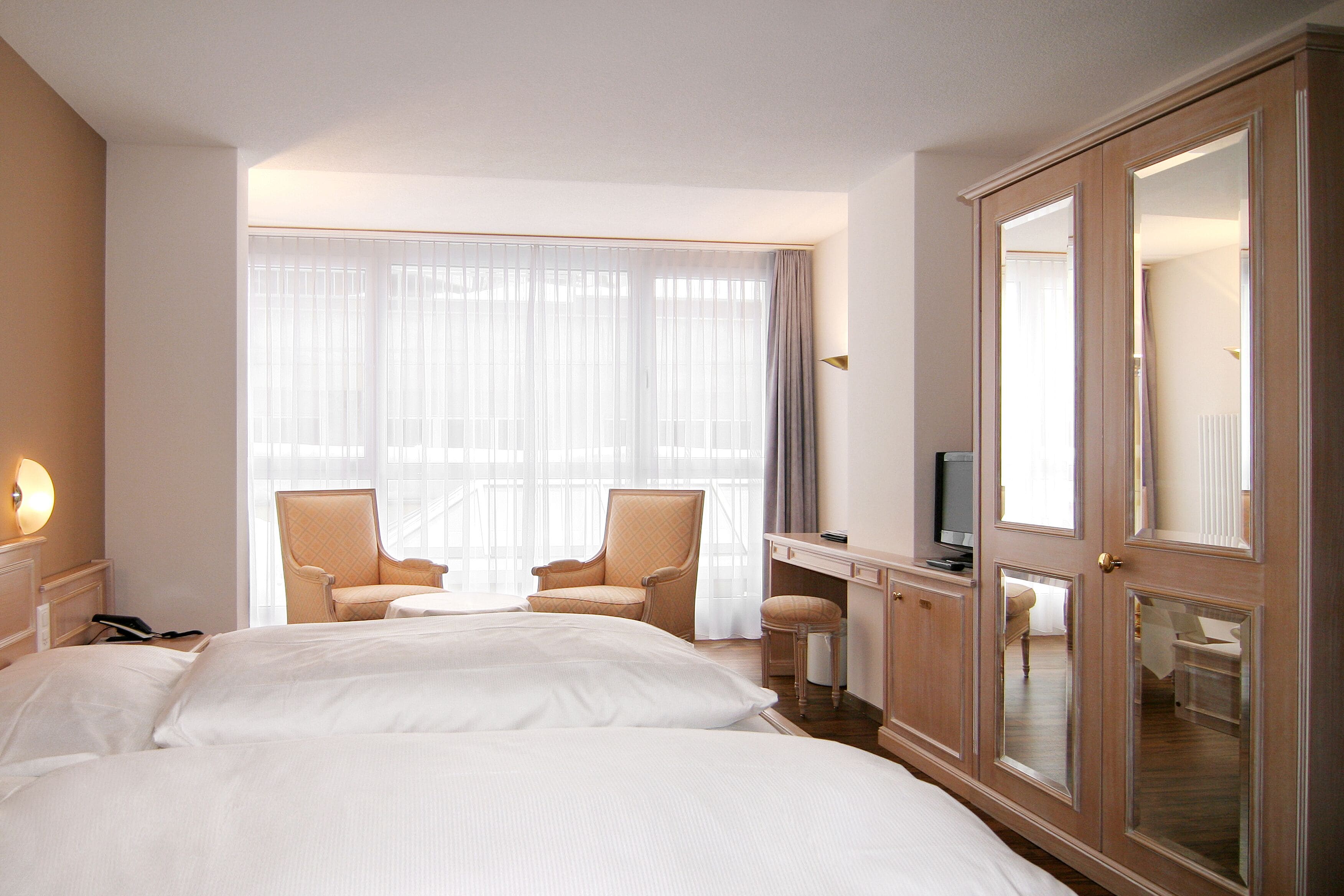 Una habitación de hotel con dos camas, un escritorio, un televisor y un armario grande.