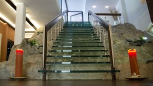 A staircase with glass steps and metal railings, flanked by two lit candles on plates, leading up to a higher floor. - Hotel Schweizerhof Gourmet & Spa (Saas-Fee)
