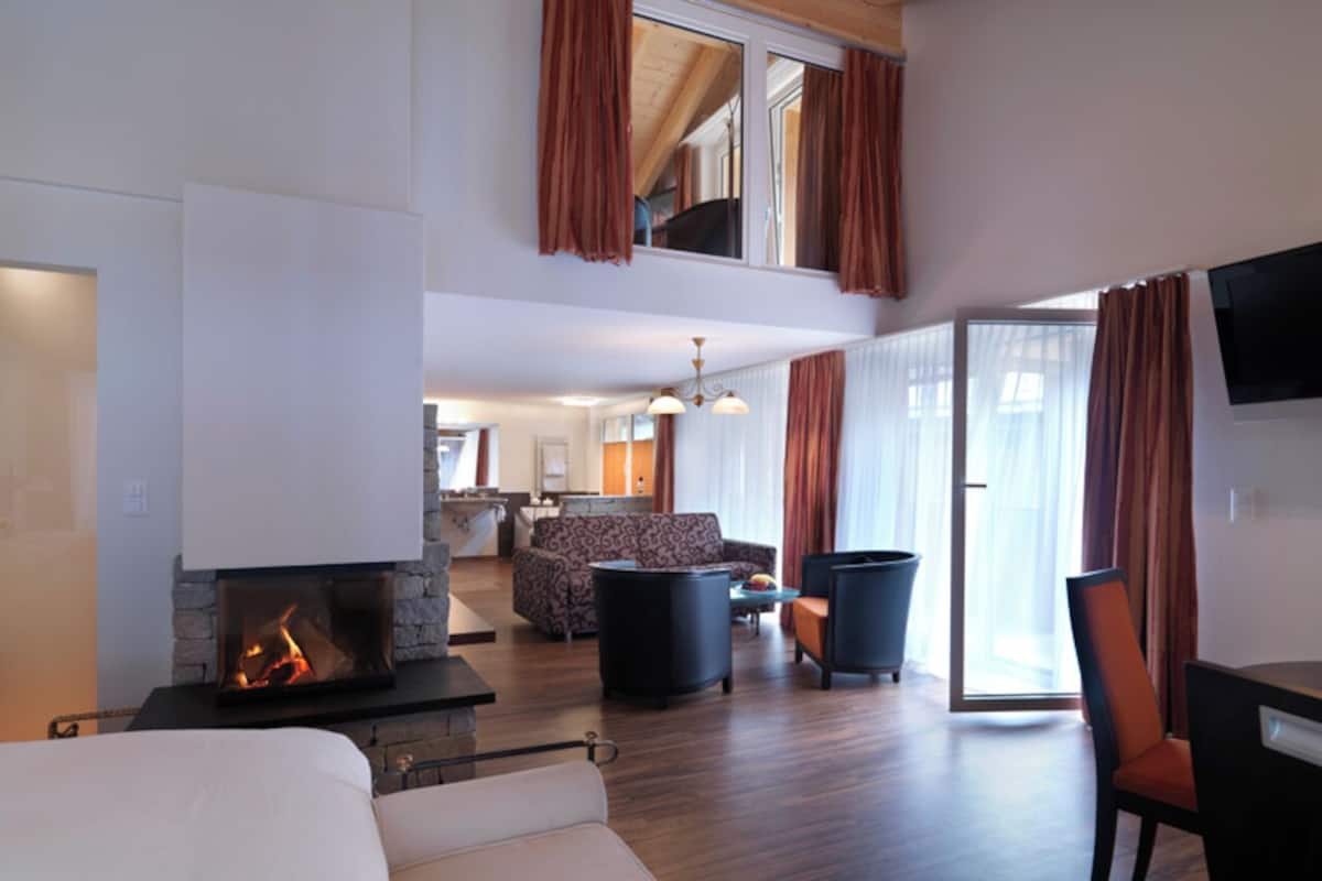Una habitación de hotel con chimenea, un sofá, una mesa de comedor y un televisor.