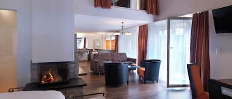 A hotel room with a fireplace, a sofa, a dining table, and a TV.
