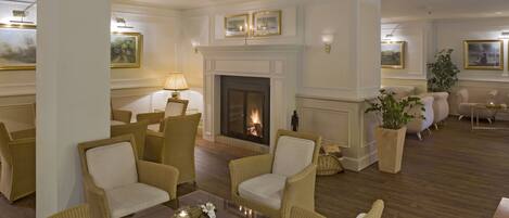 A spacious lounge with wicker furniture, a fireplace, and framed artwork on the walls.
