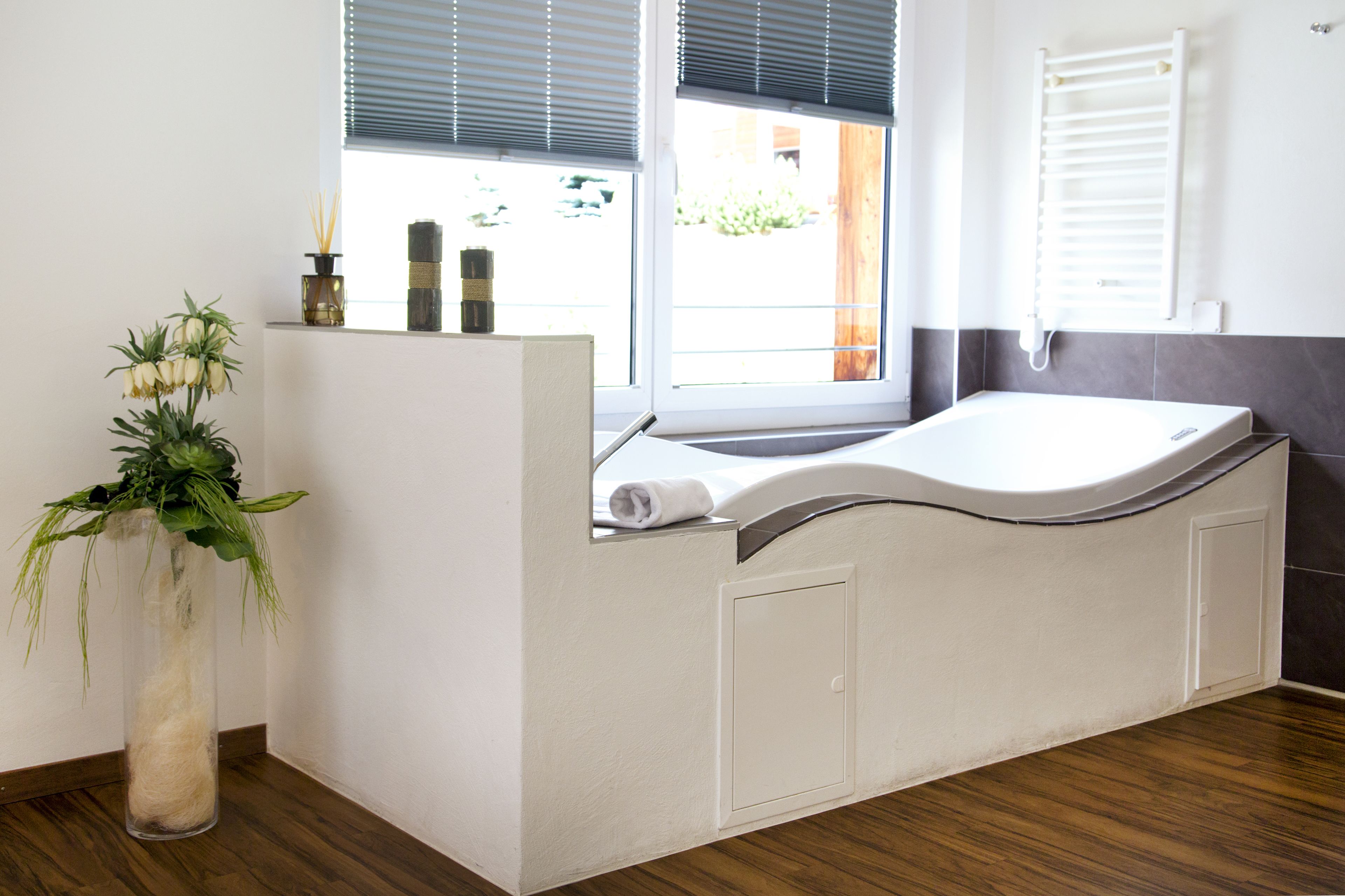 Un baño moderno con una bañera independiente, una planta en maceta y un ventanal con persianas.