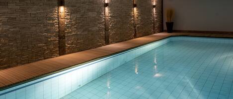 A swimming pool with tiled walls and a wooden deck.
