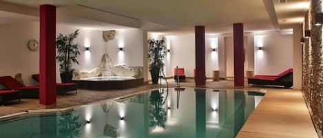 A swimming pool with red lounge chairs, a hot tub, and a wooden deck.