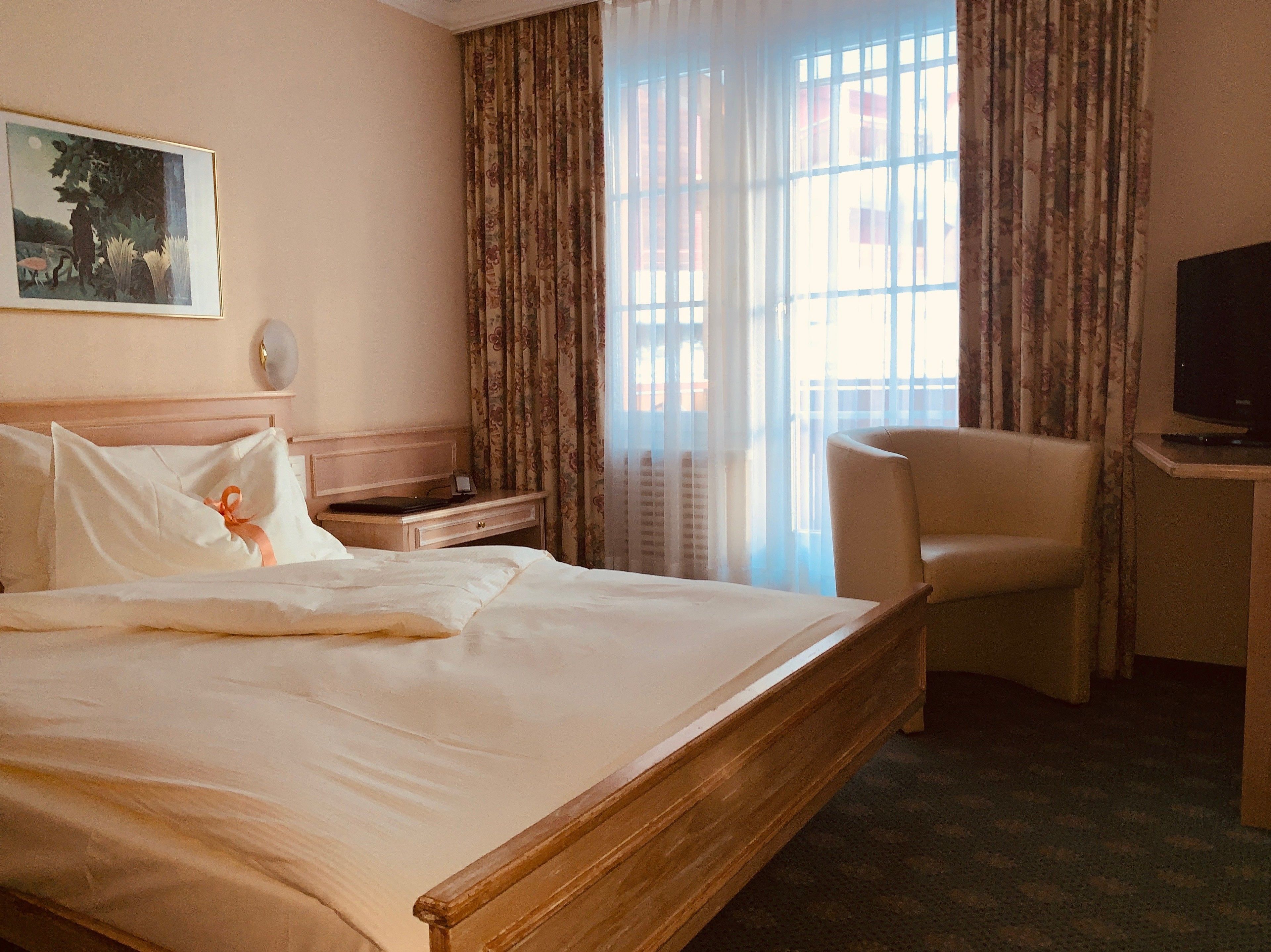 Una habitación de hotel con una cama grande, un escritorio con televisor, una silla y un cuadro en la pared.