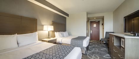 Habitación de hotel con dos camas, un escritorio, un televisor y una alfombra estampada.