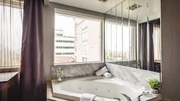 A modern bathroom with a large bathtub, a marble vanity, a window with curtains, and a mirror.