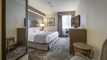 A hotel room with a bed, a desk, a chair, a television, and a mirror.