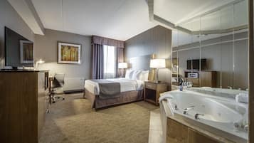 A hotel room with a large bed, a sitting area with a chair, a desk with a computer, a large mirror, and a bathtub.