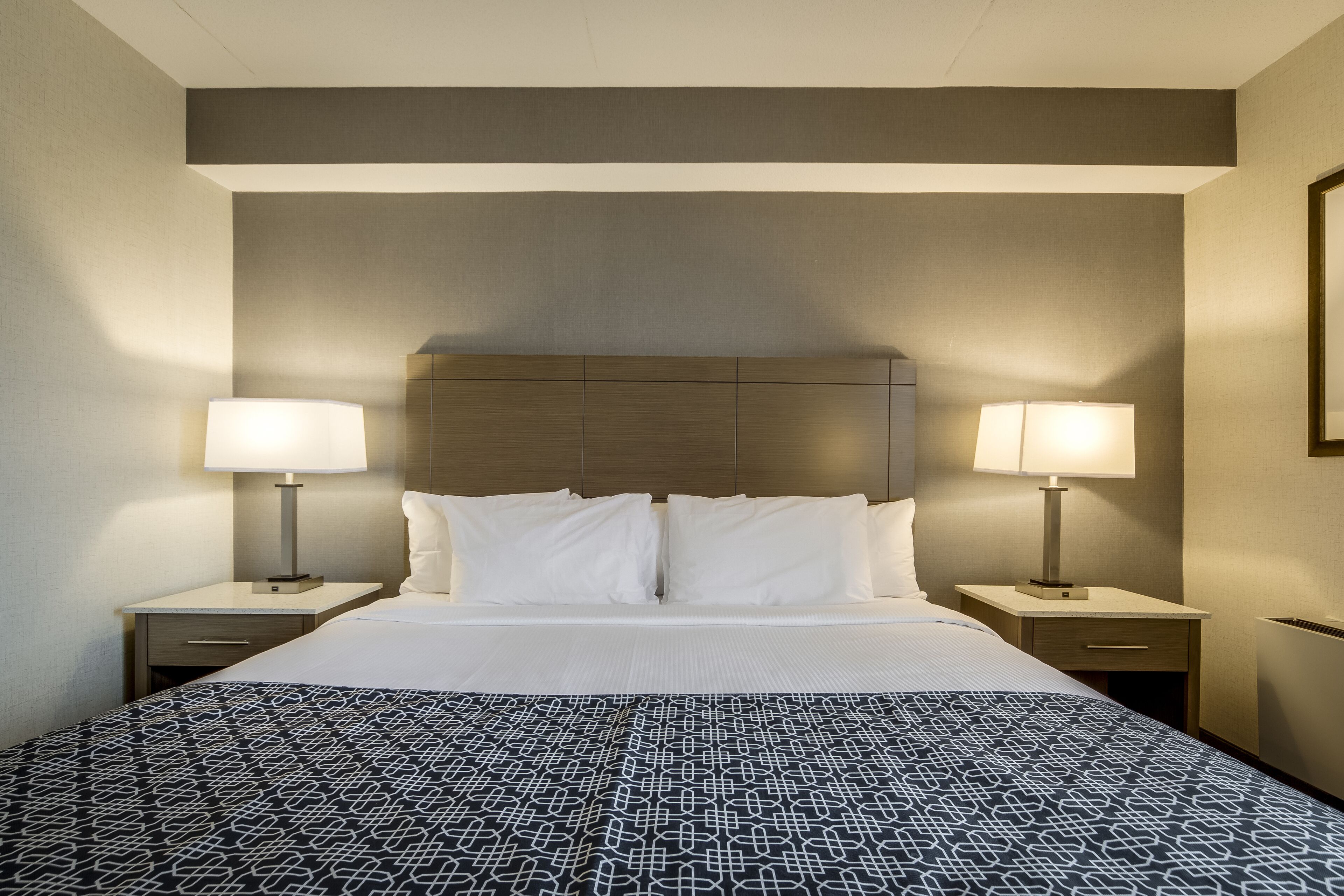 A hotel room with a large bed, two bedside tables with lamps, and a headboard.