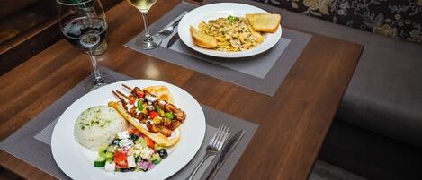 A dining table with two plates of food, a glass of white wine, and a vase with white flowers.