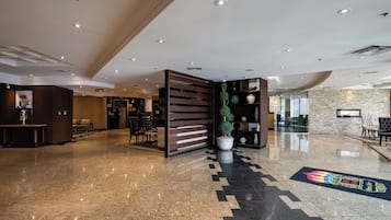 Un hall d’entrée spacieux avec un sol en marbre, un comptoir d’accueil, un espace salon et une plante décorative.