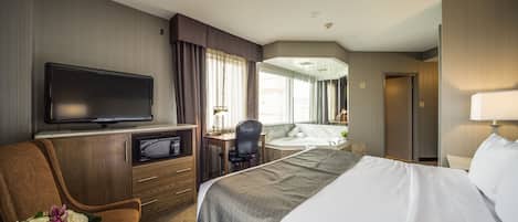 A hotel room with a large bed, a desk with a computer, a television, and a seating area with a chair and a bouquet of flowers.