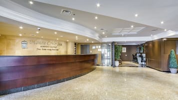 Zona de recepción de hotel con un mostrador curvo, un letrero en la pared para Monte Carlo Inn Airport Suites, una máquina expendedora y una planta en maceta.