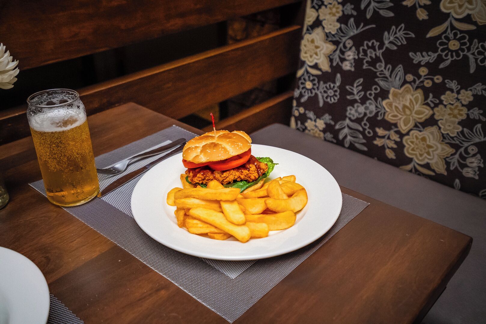 A meal consisting of a burger and fries on a white plate, accompanied by a glass of beer on a wooden table.