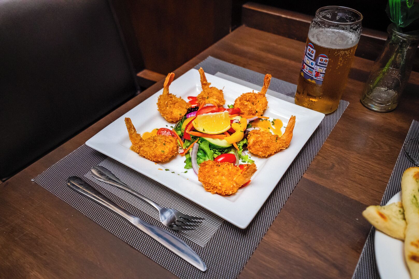 Um prato de camarões fritos com salada e um copo de cerveja sobre uma mesa de madeira.