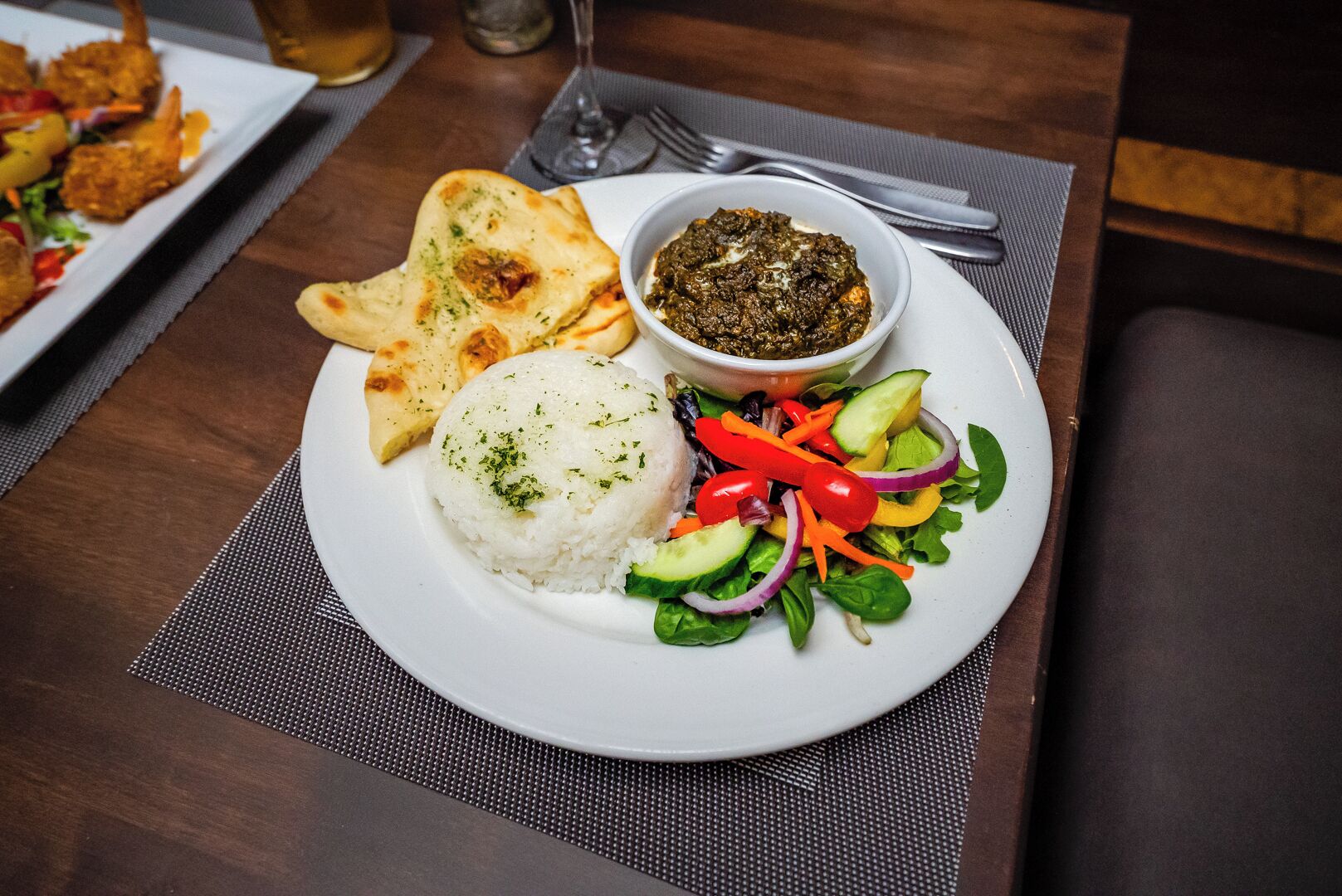 Un plato con arroz, ensalada, pan plano y un tazón de salsa.