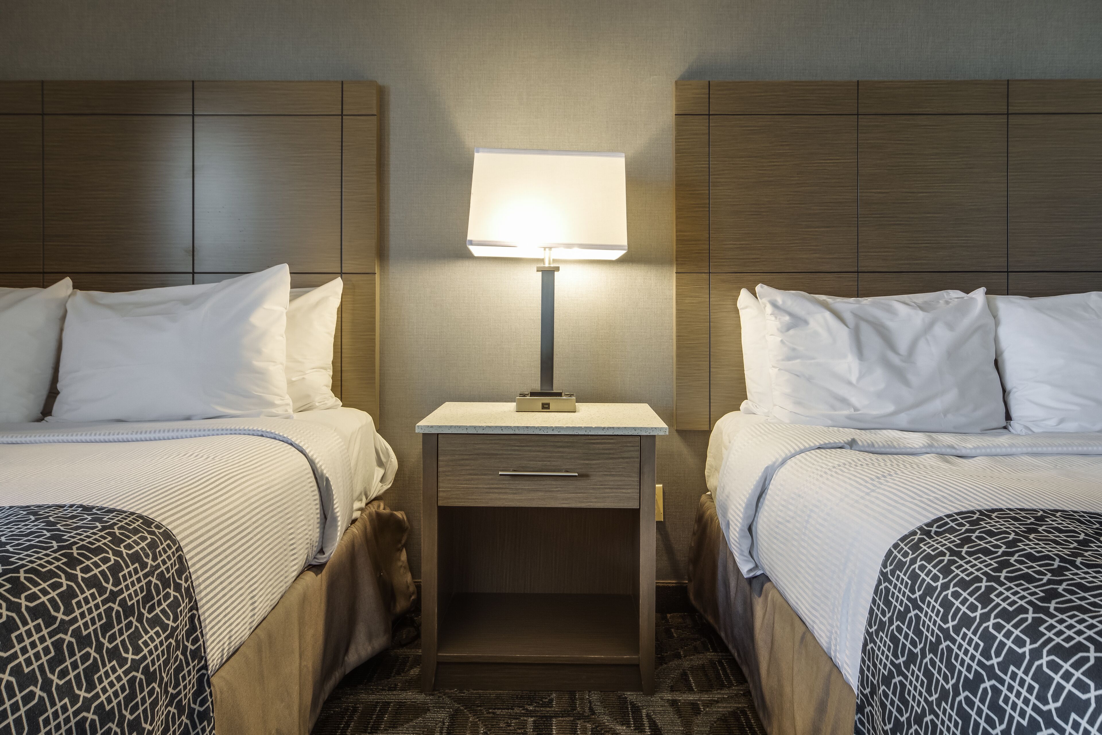 A hotel room with two beds, a nightstand with a lamp, and a drawer.