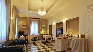 A hotel dining area with a checkered floor, a black leather sofa, tables with white tablecloths, and a chandelier. - Hotel Bagliori (Milan)