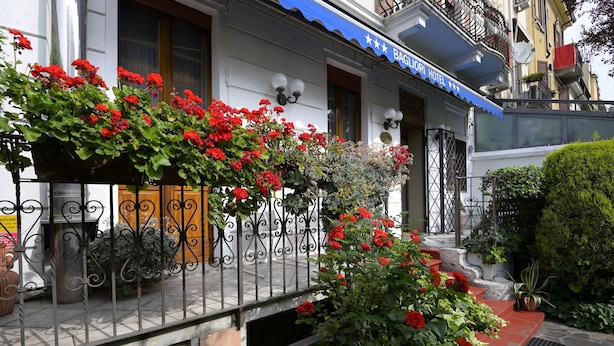 A hotel with a balcony adorned with red flowers, a blue awning, and a stone staircase leading to the entrance. - Hotel Bagliori (Milan)