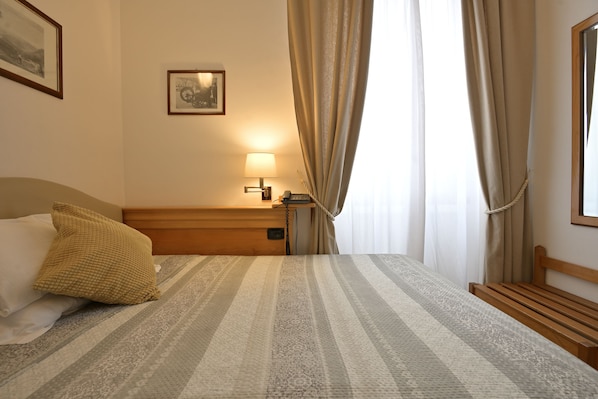 A hotel room with a bed, a bedside table, a lamp, a framed picture on the wall, and a window with curtains. - Hotel Bagliori (Milan)