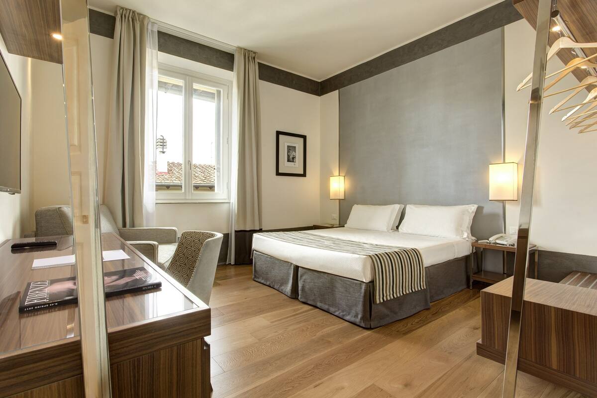 Une chambre d’hôtel comprenant un lit, une table de chevet, une lampe et un bureau avec une chaise.