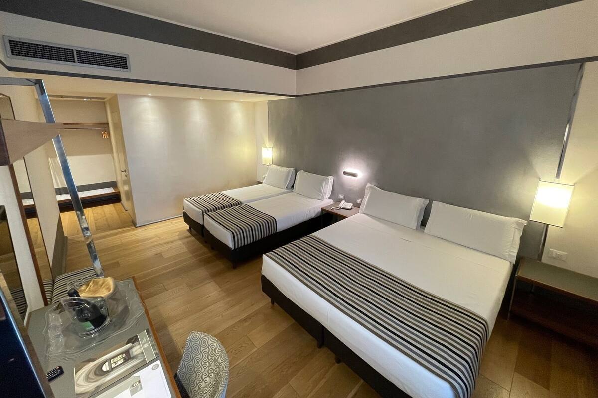 Une chambre d’hôtel avec deux lits, un bureau avec une lampe, une chaise et une petite table avec une télécommande.