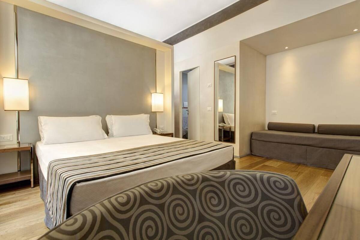 Une chambre d’hôtel moderne équipée d’un grand lit, d’un canapé, d’un bureau et d’un miroir.