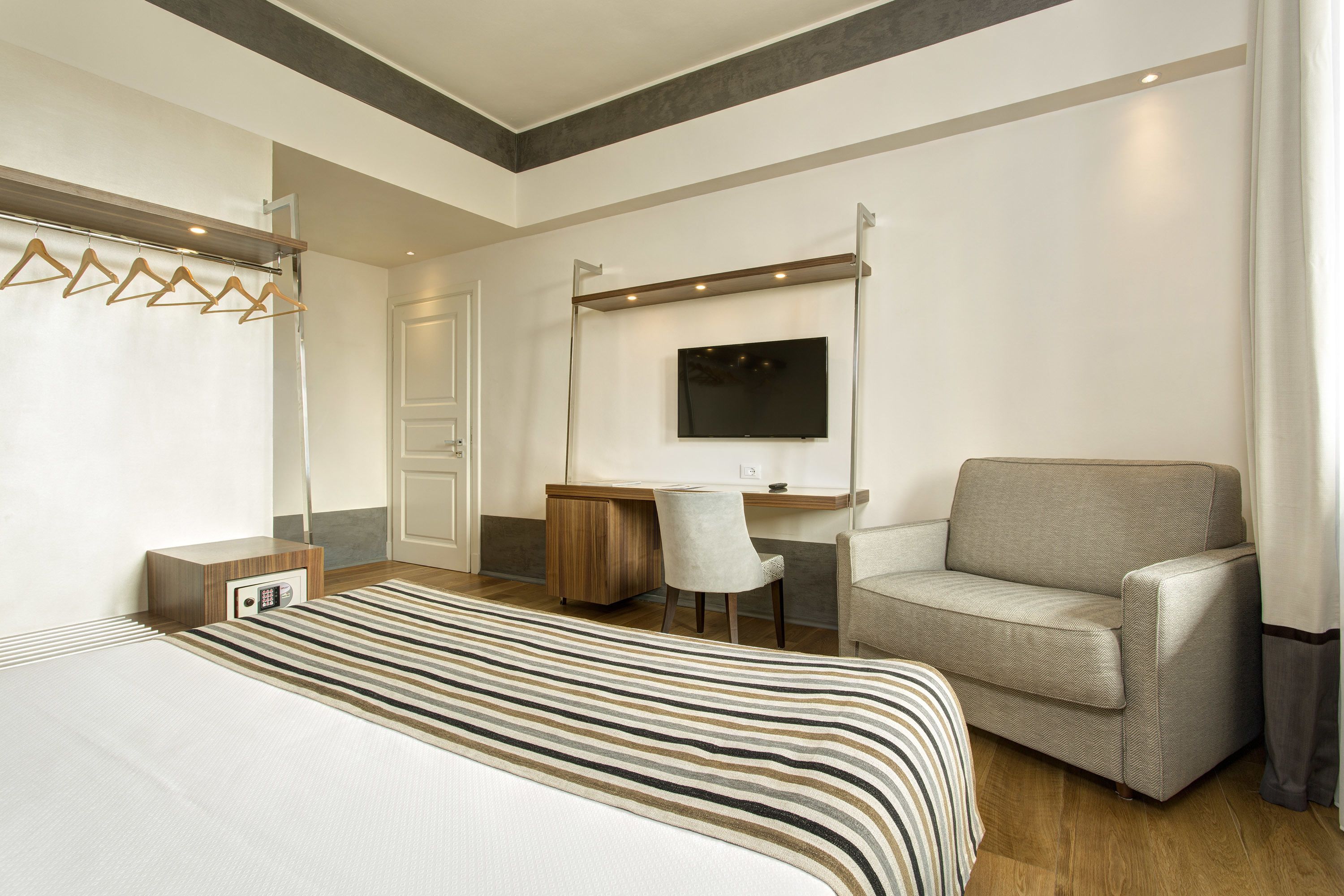 A hotel room with a bed, a desk, a chair, a TV, and a coat rack.