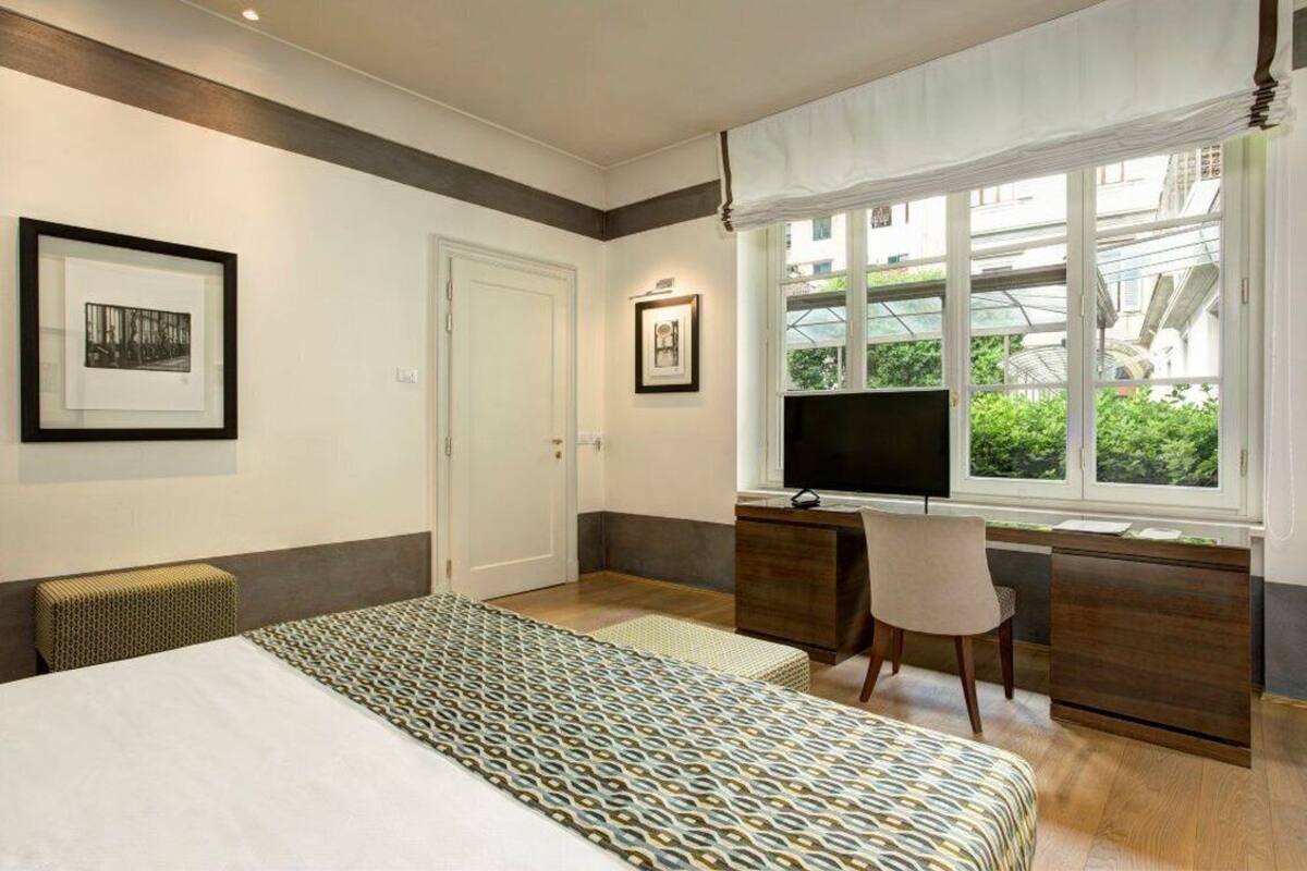 Une chambre d’hôtel avec un lit, un bureau et une chaise, une télévision et des tableaux encadrés au mur.