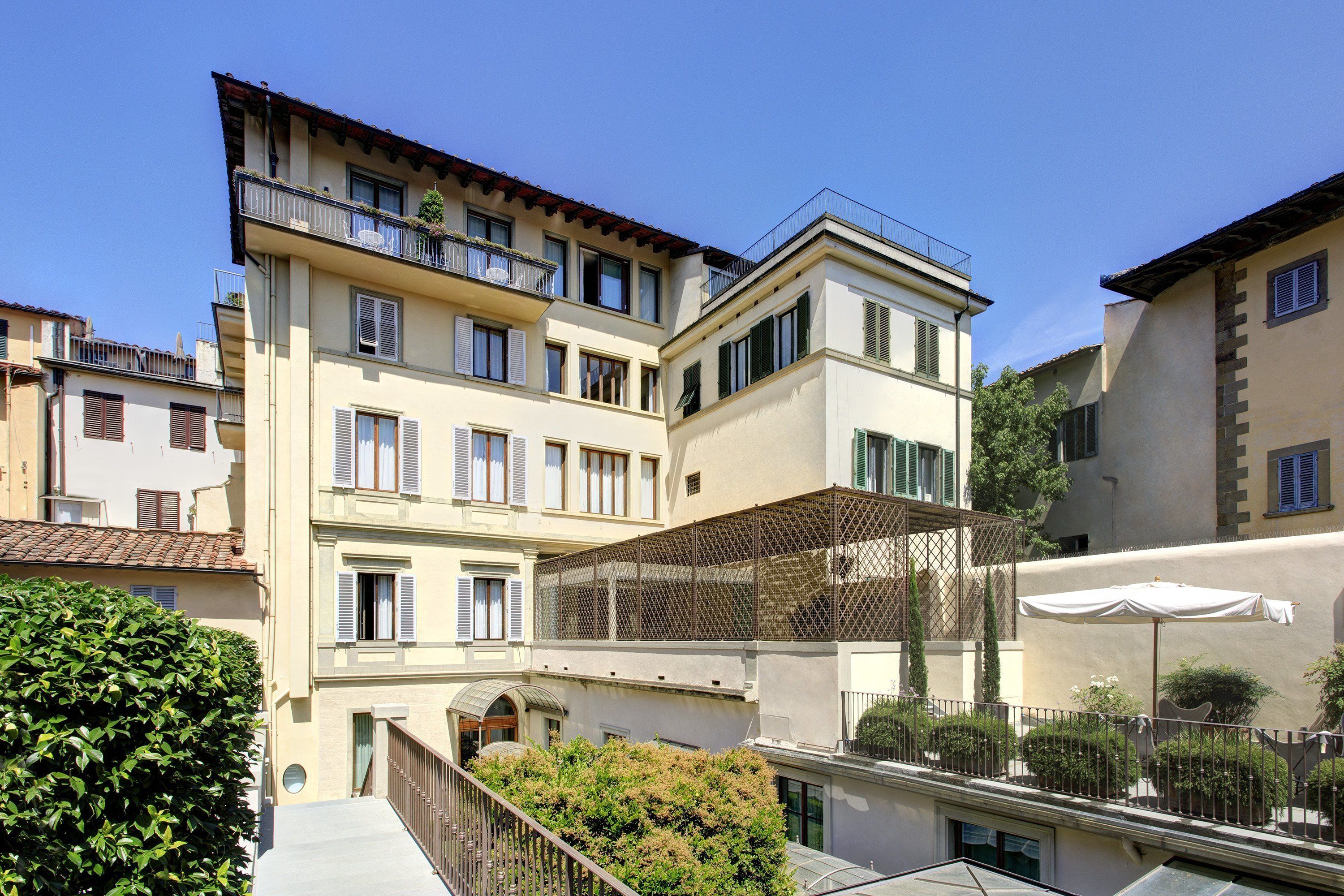 A multi-story building with balconies, a covered outdoor seating area, and a small garden.