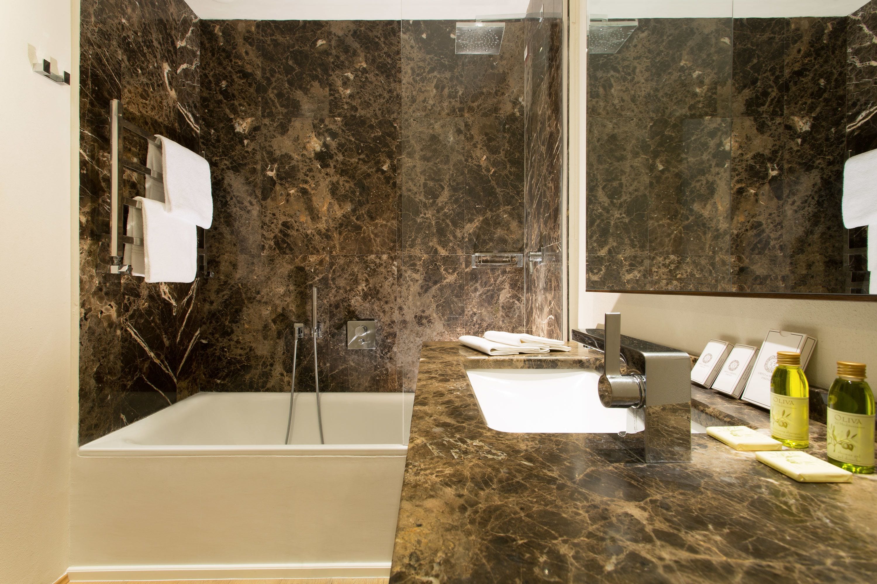 A modern bathroom with a marble countertop, a bathtub, a large mirror, and toiletries.