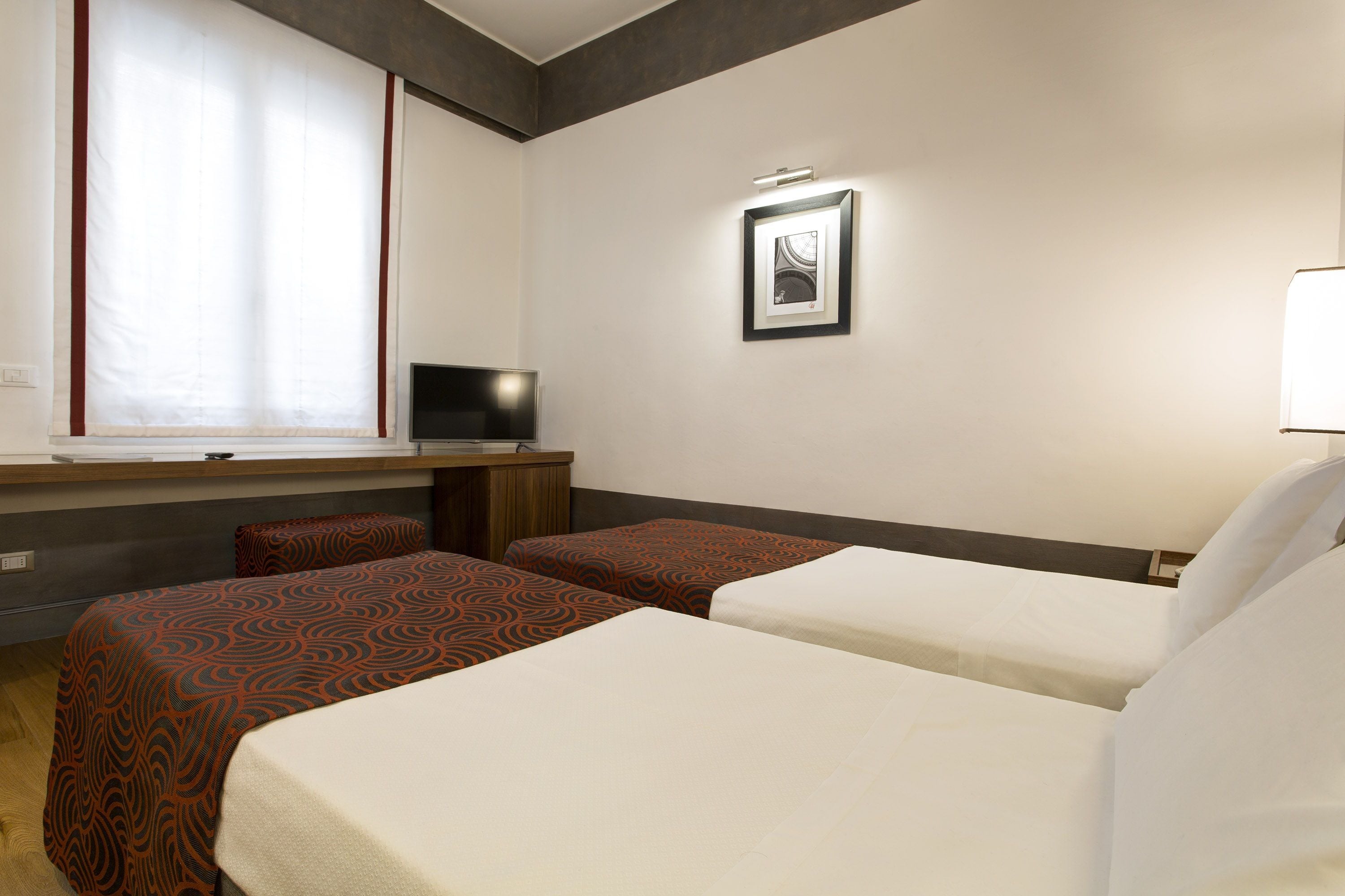 A hotel room with two beds, a desk, a TV, and a framed picture on the wall.