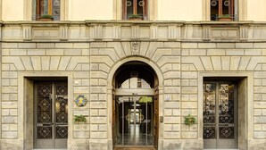 Um edifício histórico com uma entrada central em arco, duas portas simétricas com detalhada ferragem e uma placa indicando o nome do edifício.