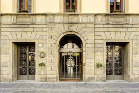 A historic building with a central arched entrance, two symmetrical doors with intricate metalwork, and a plaque indicating the building's name.