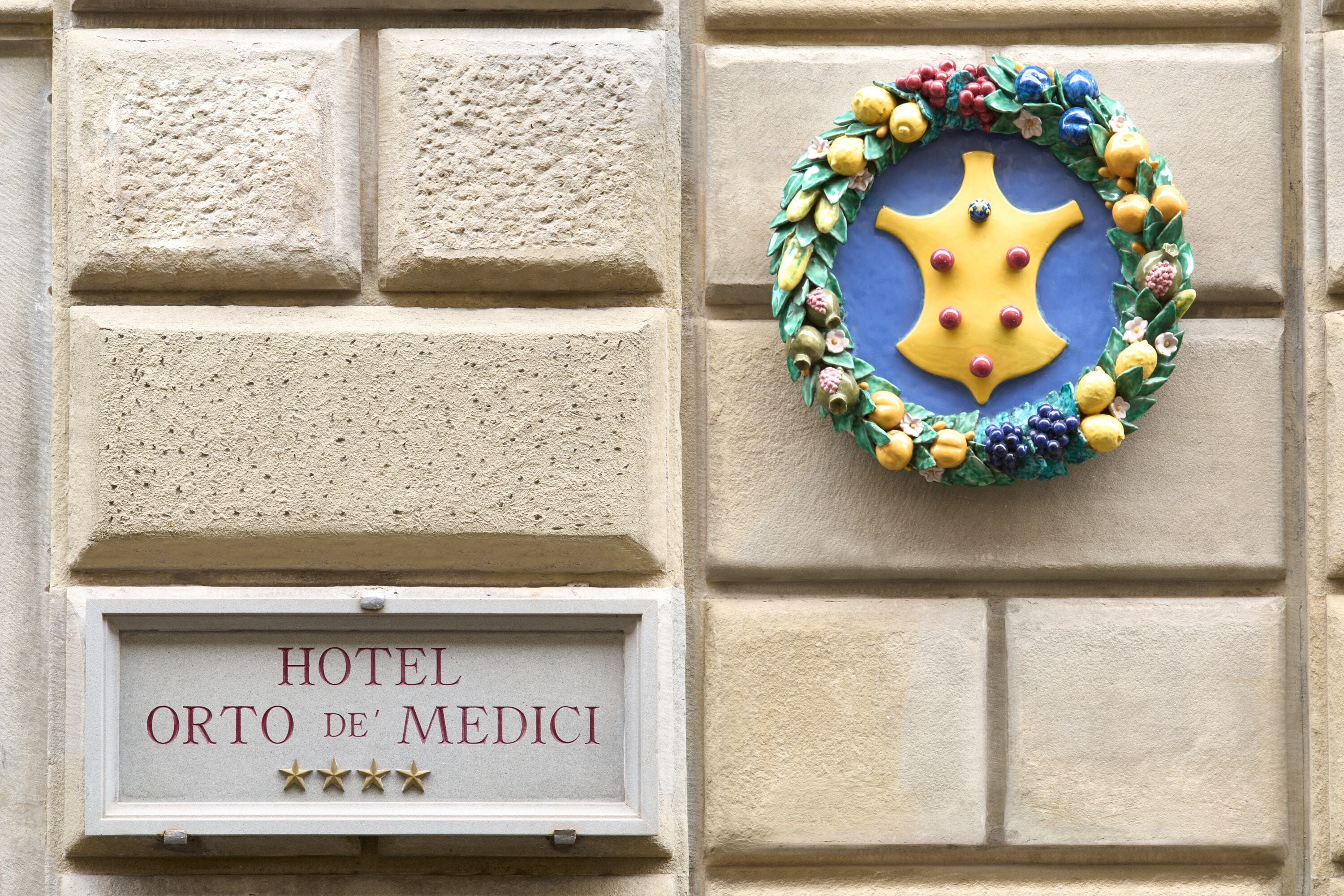 Placa de hotel com o nome 'HOTEL ORTO DE' MEDICI' e uma grinalda decorativa com um biscoito em forma de estrela.