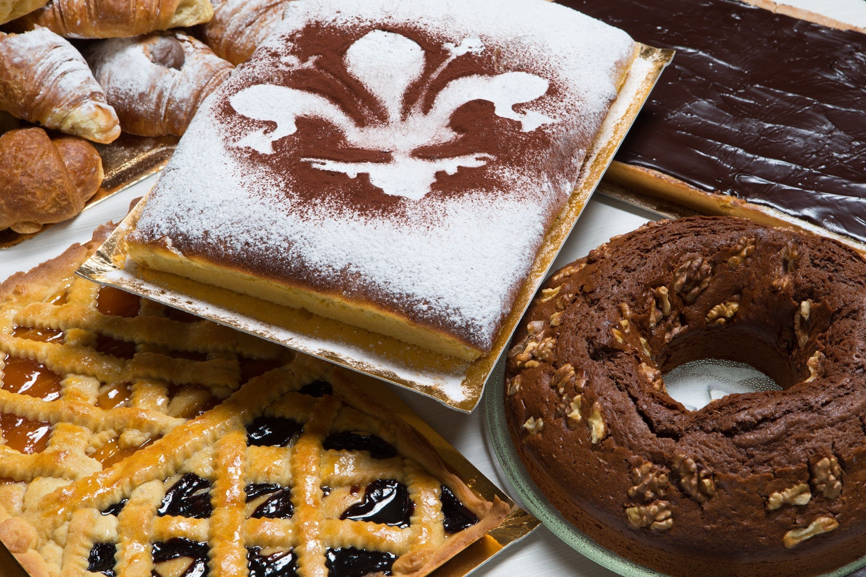 Variedad de productos horneados, incluyendo un pastel con azúcar glas, una tarta de corteza entrecruzada, un bizcocho de chocolate y una rosquilla con nueces.