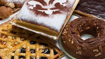 Variedad de productos horneados, incluyendo un pastel con azúcar glas, una tarta de corteza entrecruzada, un bizcocho de chocolate y una rosquilla con nueces.