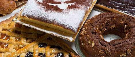 Variedad de productos horneados, incluyendo un pastel con azúcar glas, una tarta de corteza entrecruzada, un bizcocho de chocolate y una rosquilla con nueces.