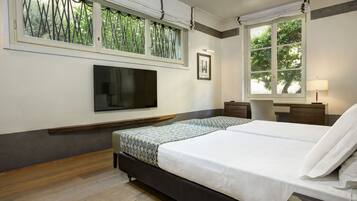 Un dormitorio con una cama grande, un televisor montado en la pared, una ventana con vistas a árboles y una mesita de noche con una lámpara.