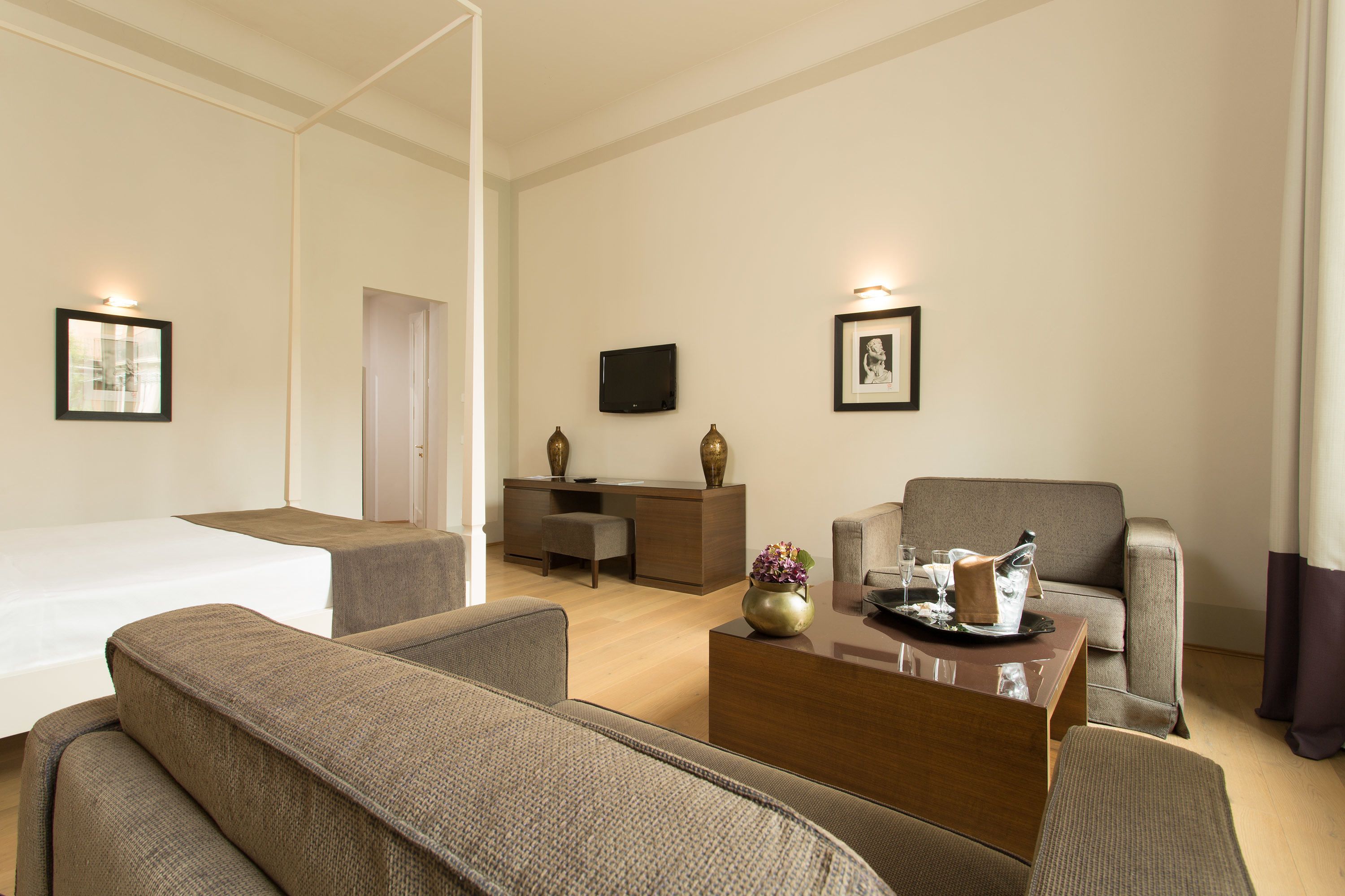 A modern hotel room with a bed, two sofas, a coffee table, a TV, and framed pictures on the walls.