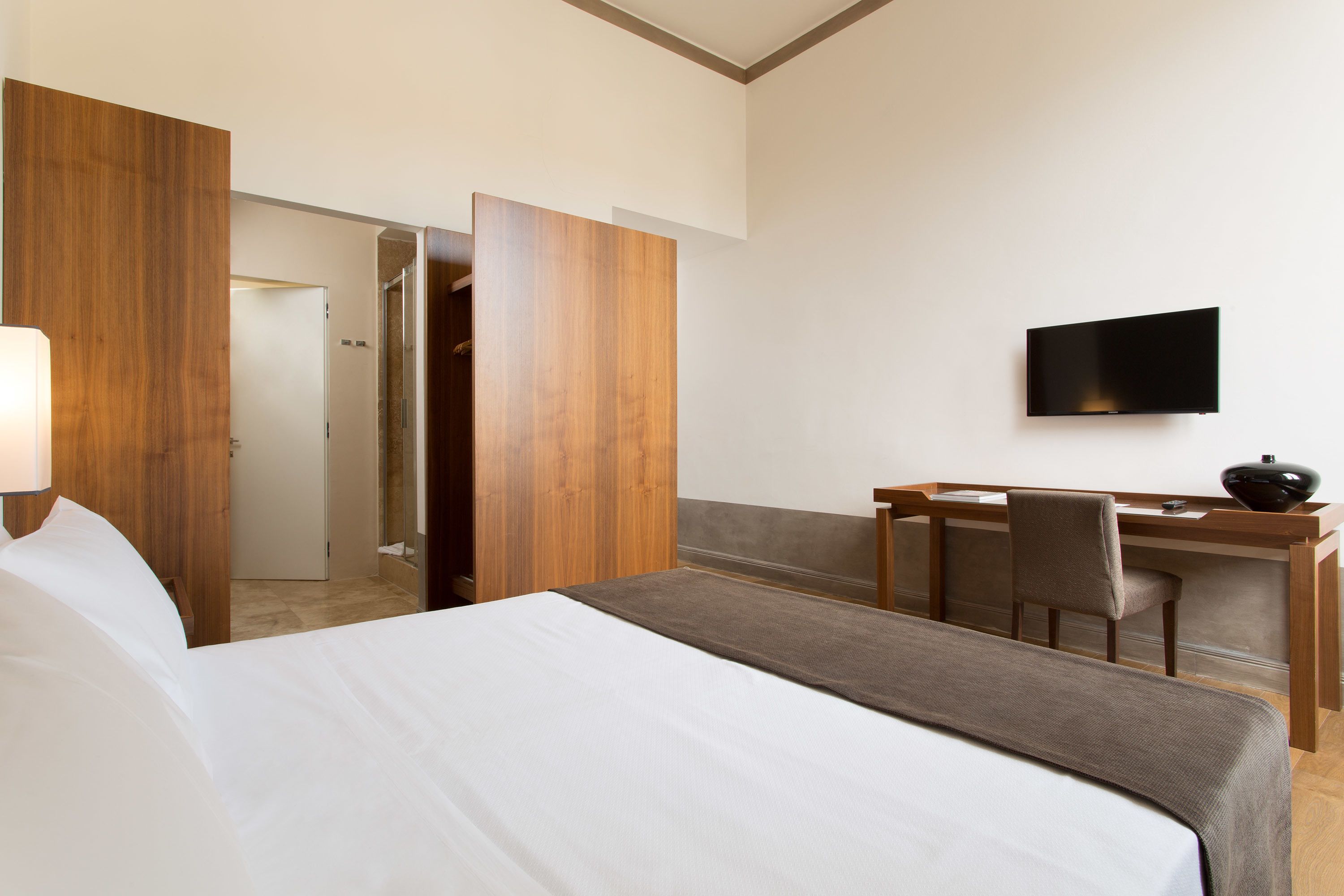 A hotel room with a bed, a desk, a chair, and a television on the wall.