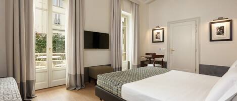 A bedroom with a large bed, a flat-screen TV mounted on the wall, a small table with chairs, and a window with curtains.