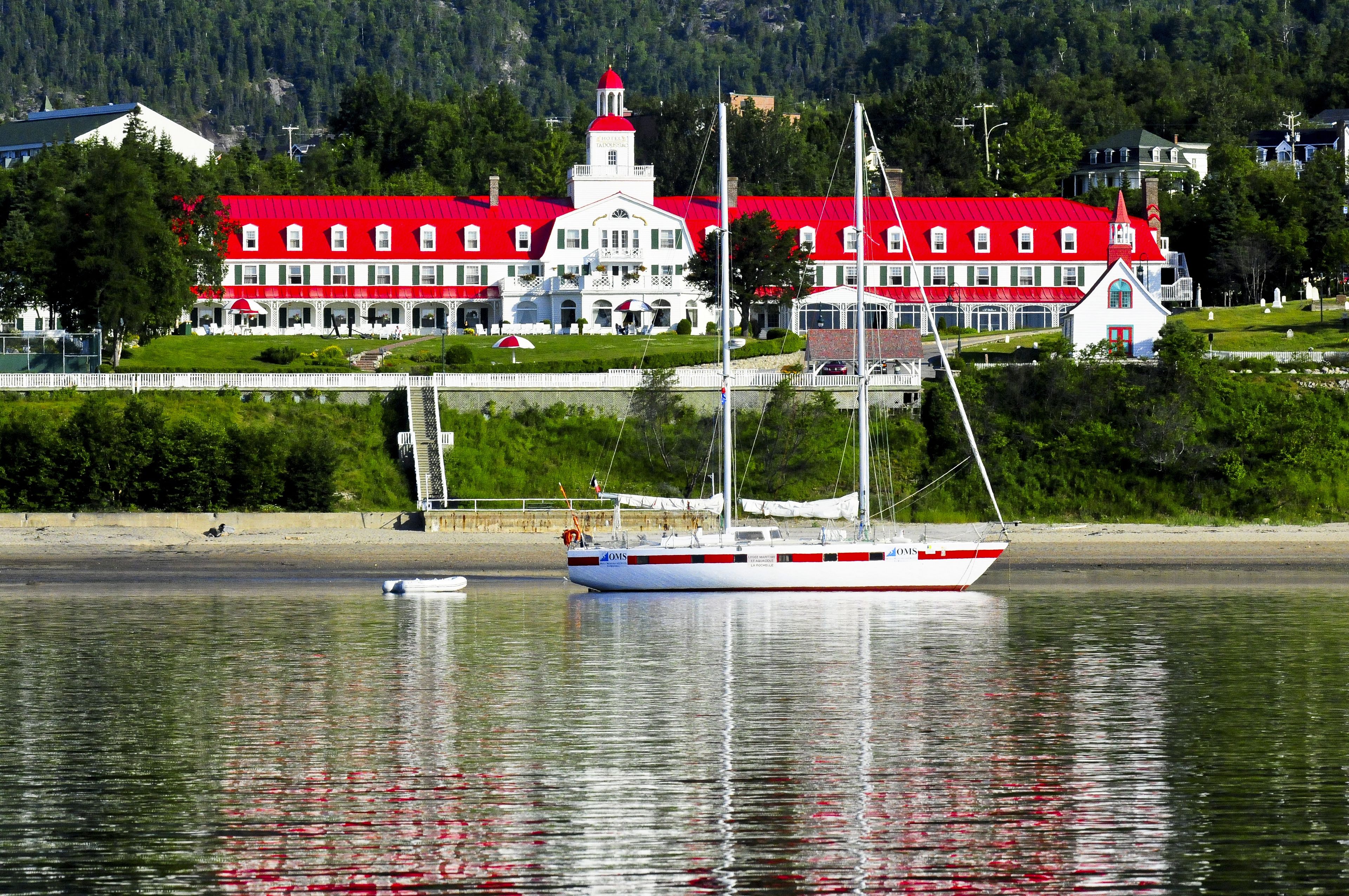 Un edificio grande de color blanco con techo rojo y una torre, ubicado junto a una masa de agua tranquila.