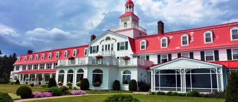 A large, multi-story building with a red roof and white walls, featuring a prominent tower with a cross on top.