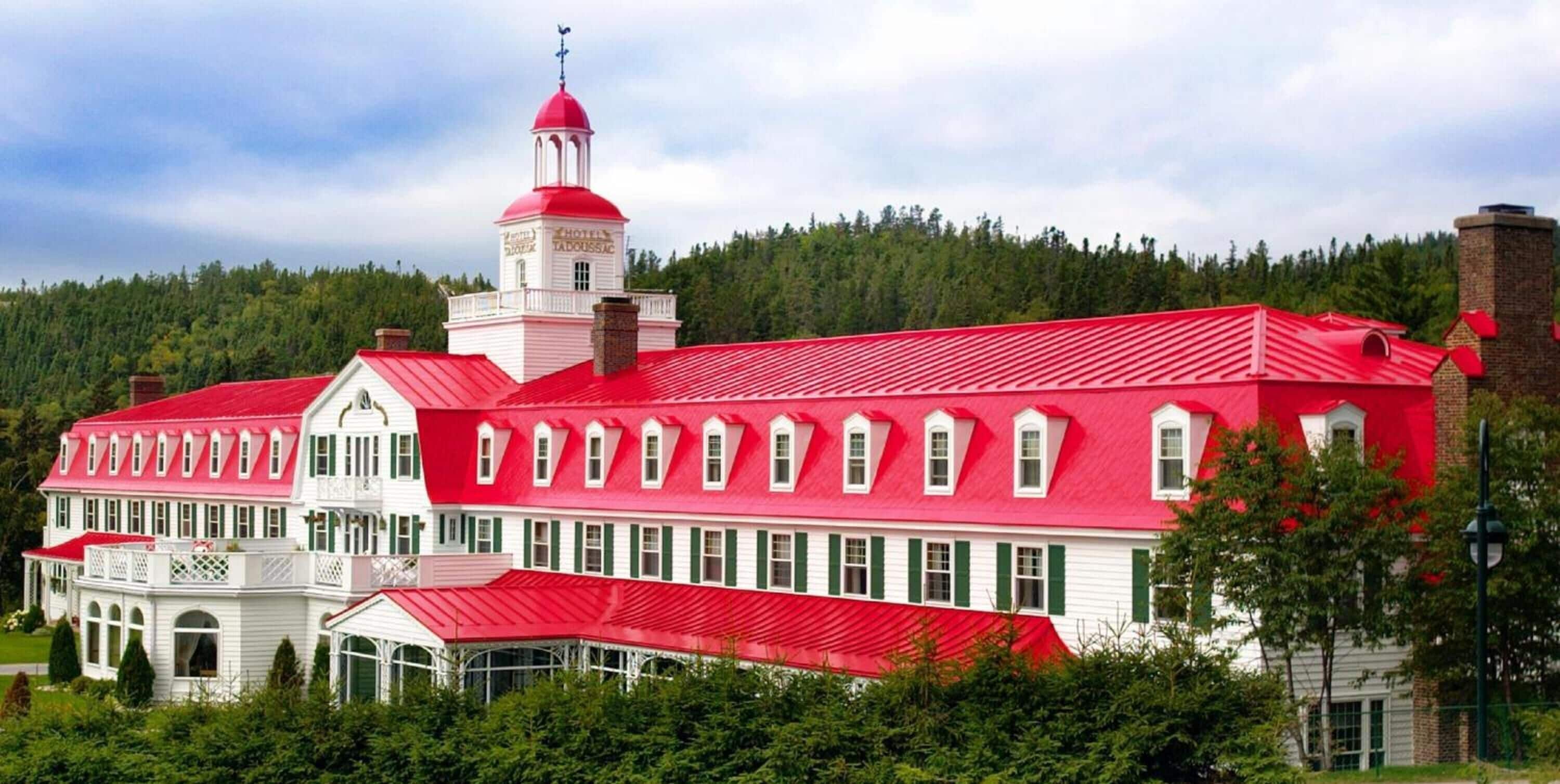 A large building with a red roof and white walls, featuring a bell tower and multiple windows.